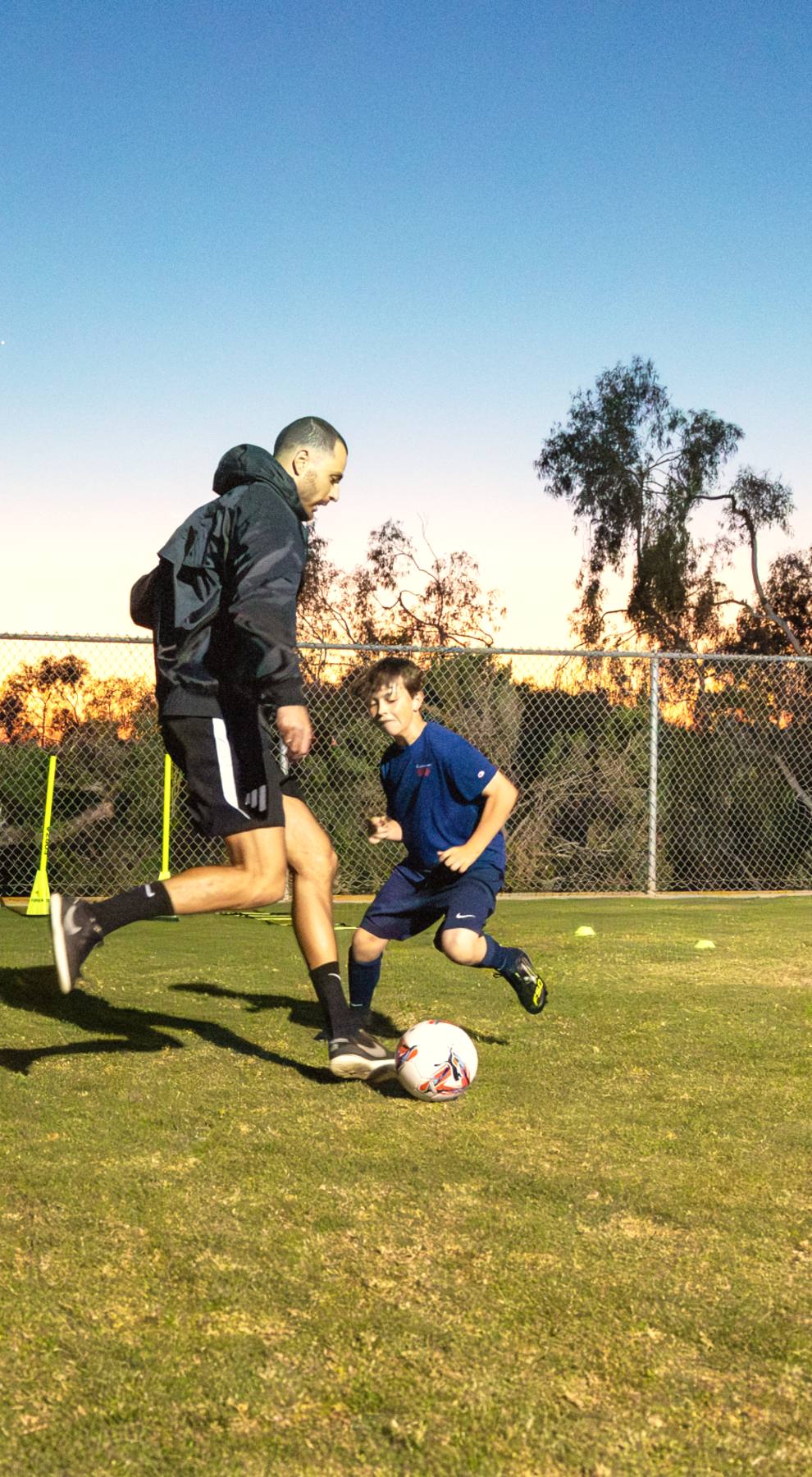 A player shields the ball from Coach Luka in a 1v1 duel at dusk, individual training for club players at The Soccer Lab, Carlsbad